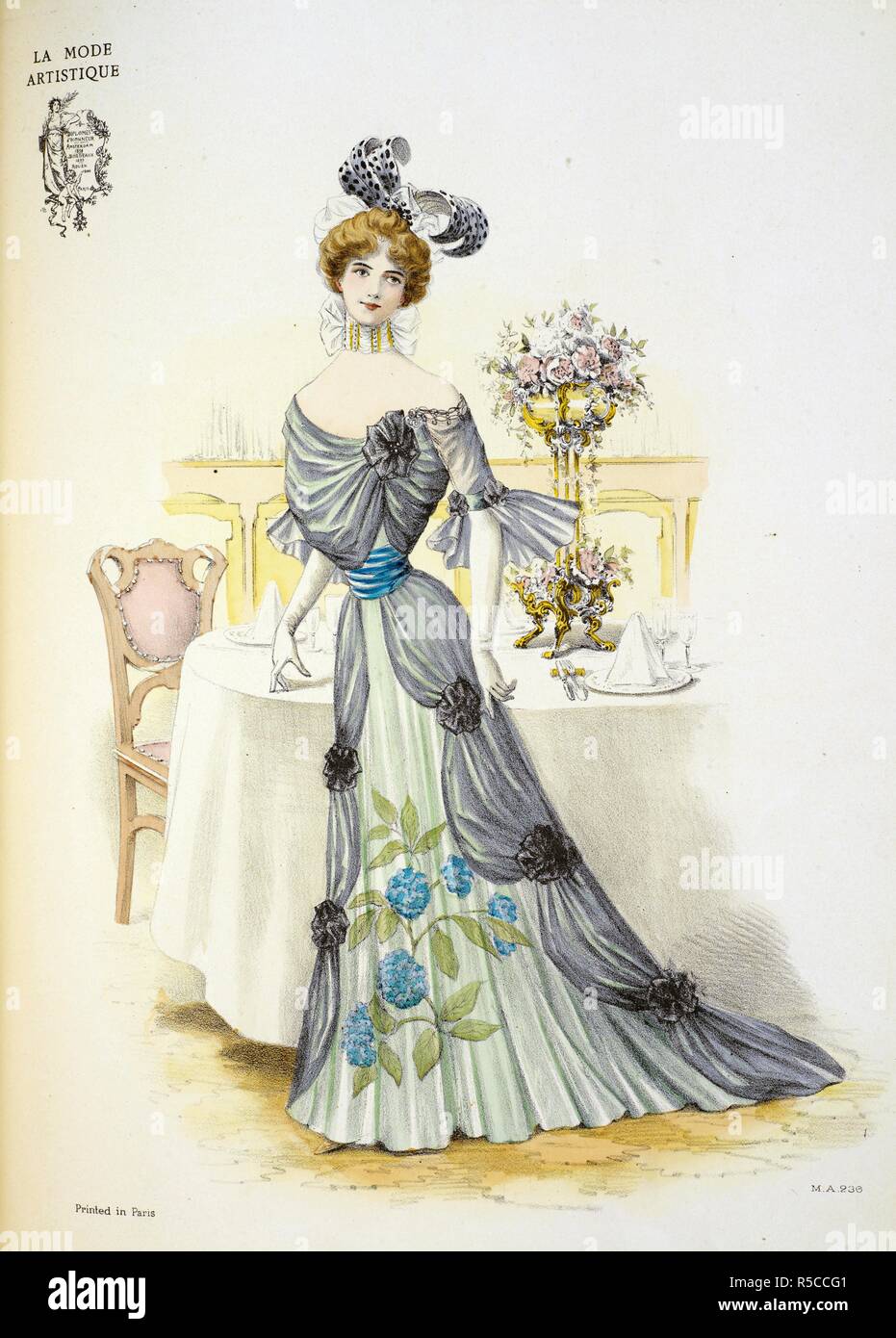 Design by Barroin. An evening dress. It is made of black mousseline de soie, the over-skirt draped back in festoons which are caught up at intervals with full rosettes of black velvet. It opens over a petticoat of white satin veiled with pleated mousseline in a shade of green, upon which is painted a cluster of hortensias. The corsage is draped to match the skirt, a belt of blue satin encircling the waist. The head-dress is particularly striking: a mere rien of white velvet, the quills studded with black paillettes and caught together with a large jet ornament. The Powder Puff [An English edit Stock Photo