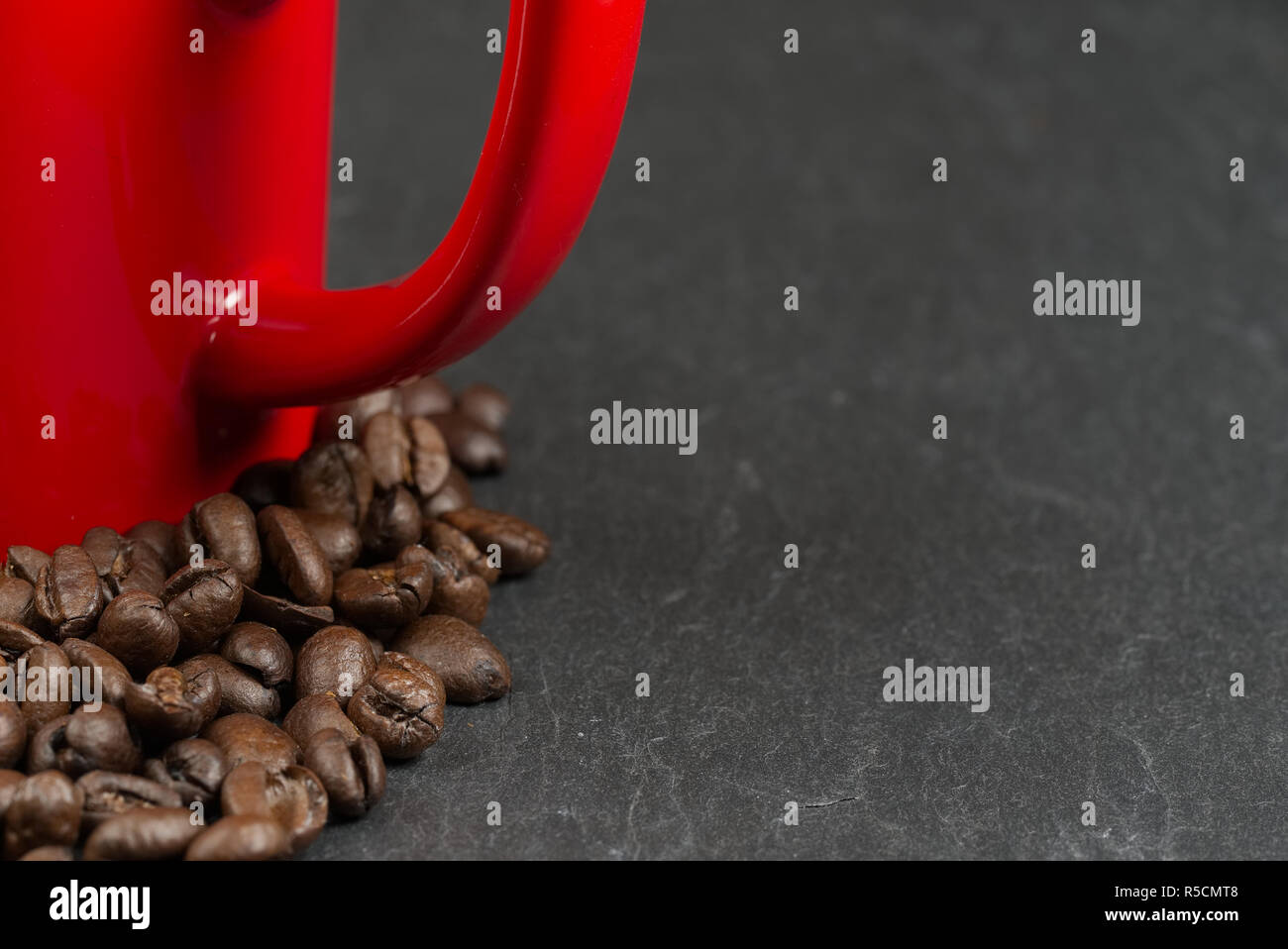 Coffee beans surrounding a red mug on a slate background with shallow depth of field. Love coffee concept Stock Photo