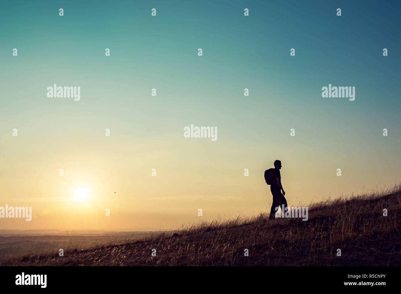 A silhouette of a lone man with a rucksack walking up a hill with the