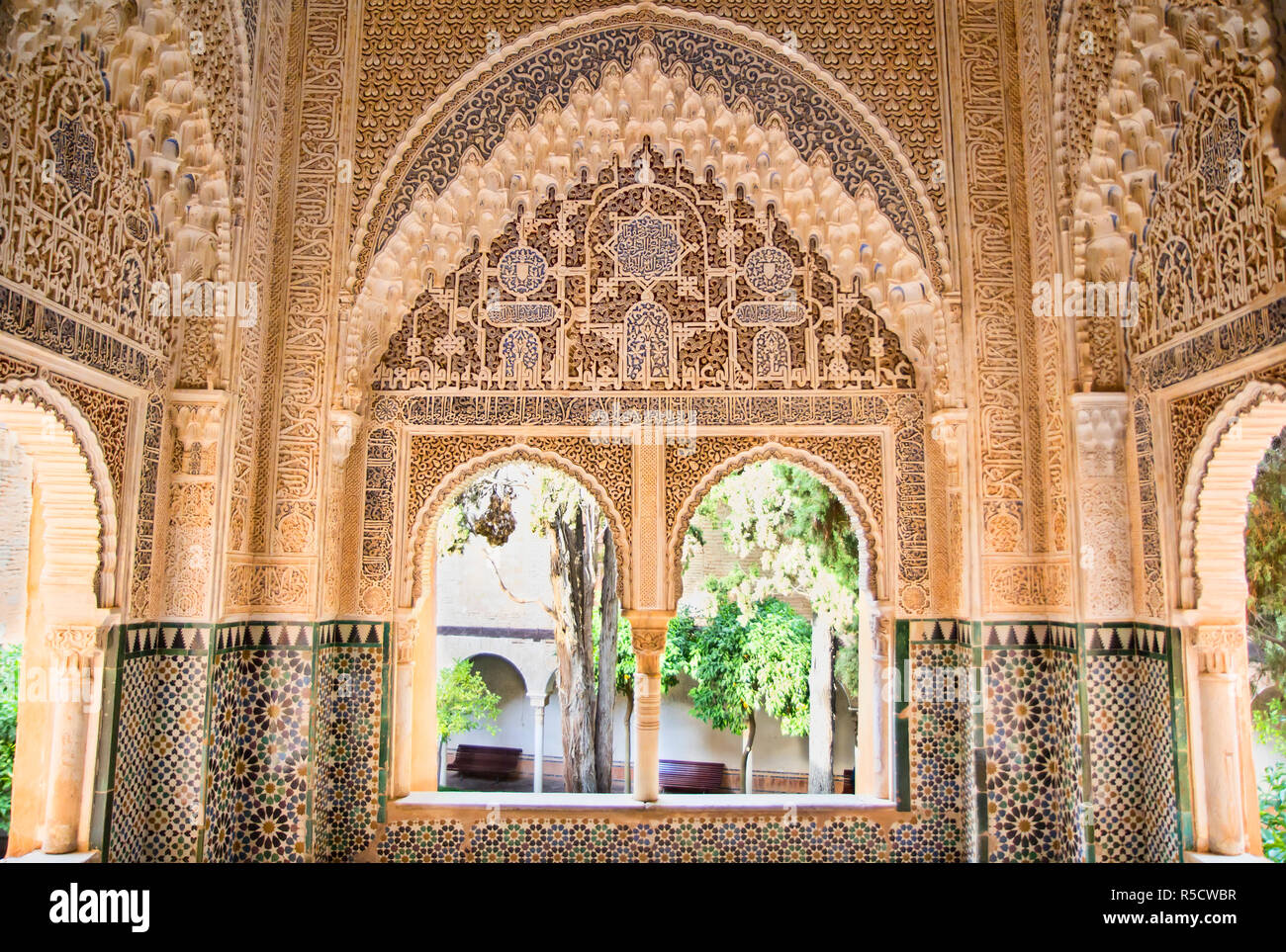 Moorish architecture in the Nasrid Palaces of the Alhambra of Granada in Spain, with beautiful intricate carvings and windows ovrlooking a garden. Stock Photo