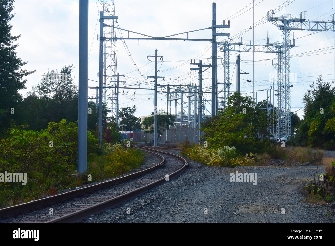 High voltage electrical power tower and cables over railroad tracks on a partly cloudy day Stock Photo
