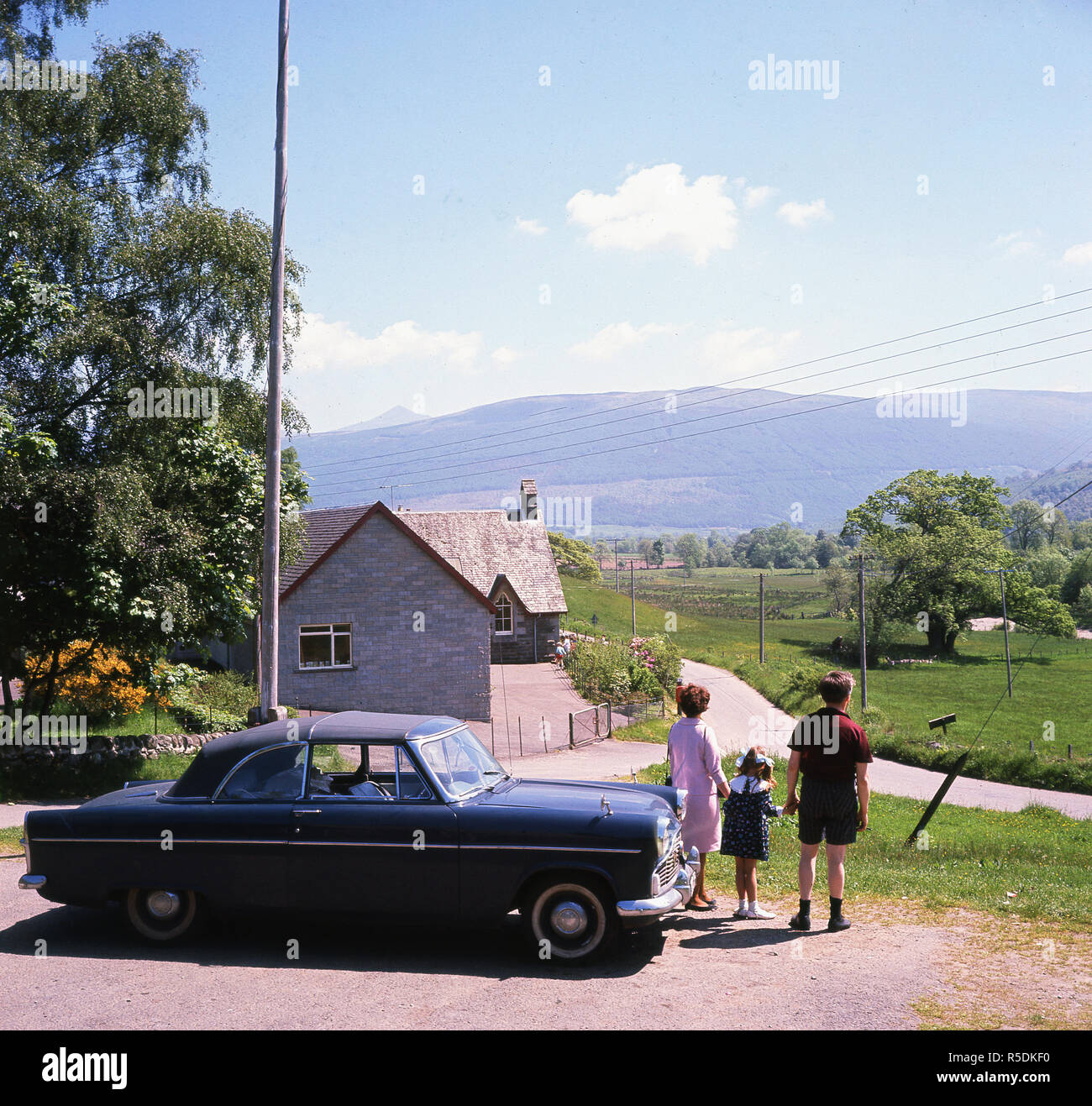 1960s, Balquhidder, Stirling, Scotland, a couple and their small child stand by their car looking at the mountain terrain of the Braes of Balquhidder that overlooks the village. The famous Scottish outlaw and folk hero, Rob Roy lived and died in Balquhidder. Stock Photo
