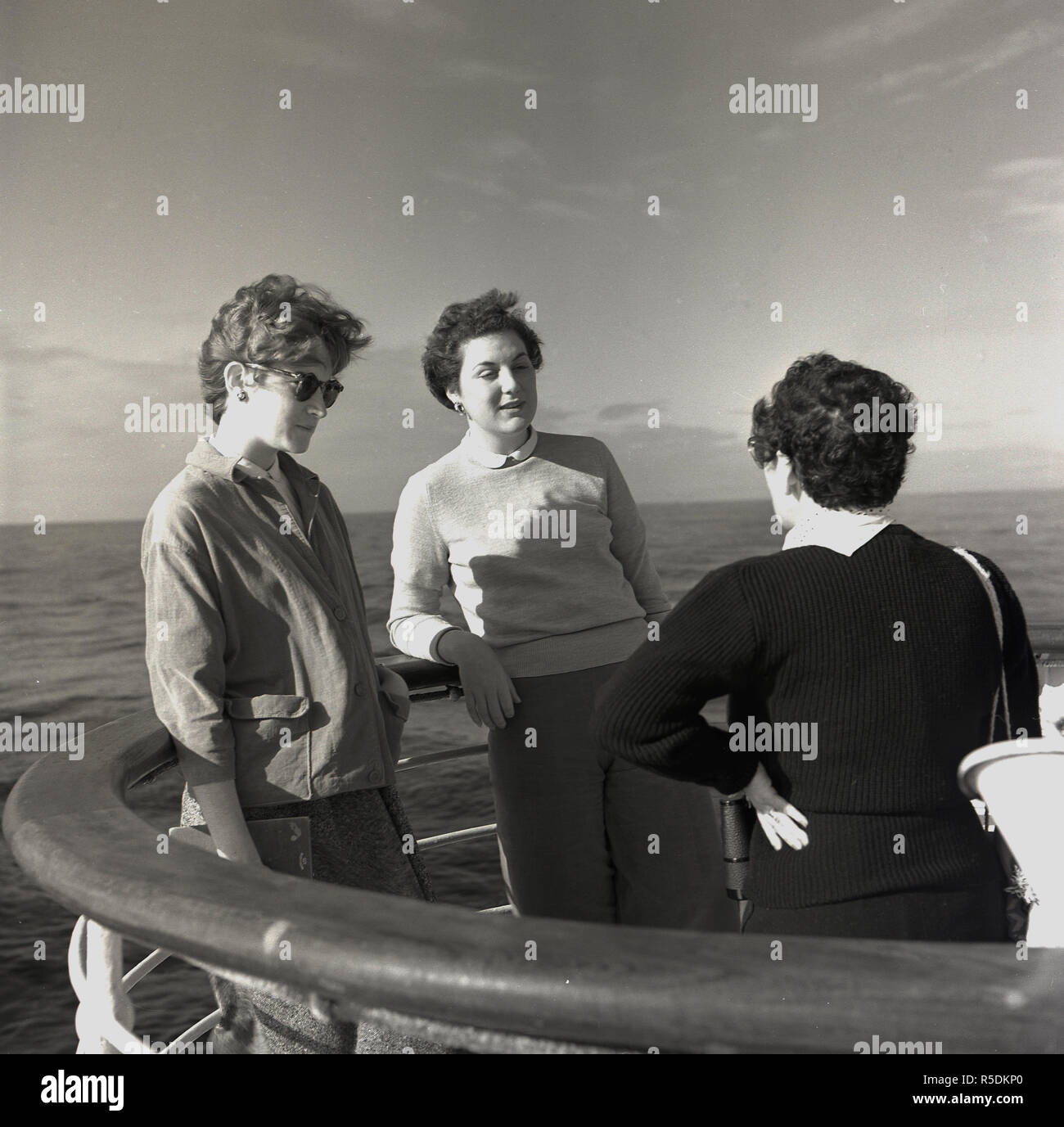1960, mid-ocean and on a union-castle steamship headed for the Cape in South Africa, two young women have a discussion with an older female traveller in a corner of the ship's outer deck. Stock Photo