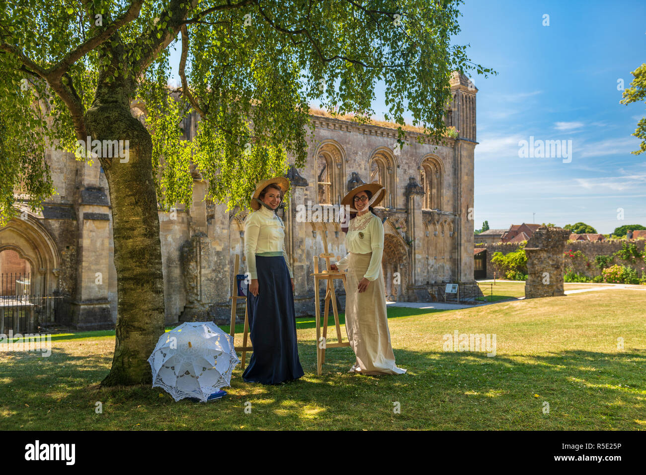 Two young ladies in Edwardian period costumes pose with their easels on a summers day at the historic abbey in Glastonbury, Somerset. Stock Photo