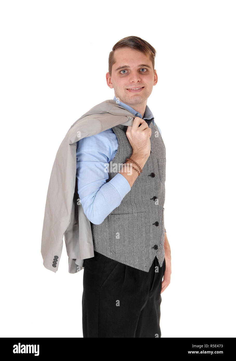 A handsome young man standing in a gray vest and dark pants with his ...