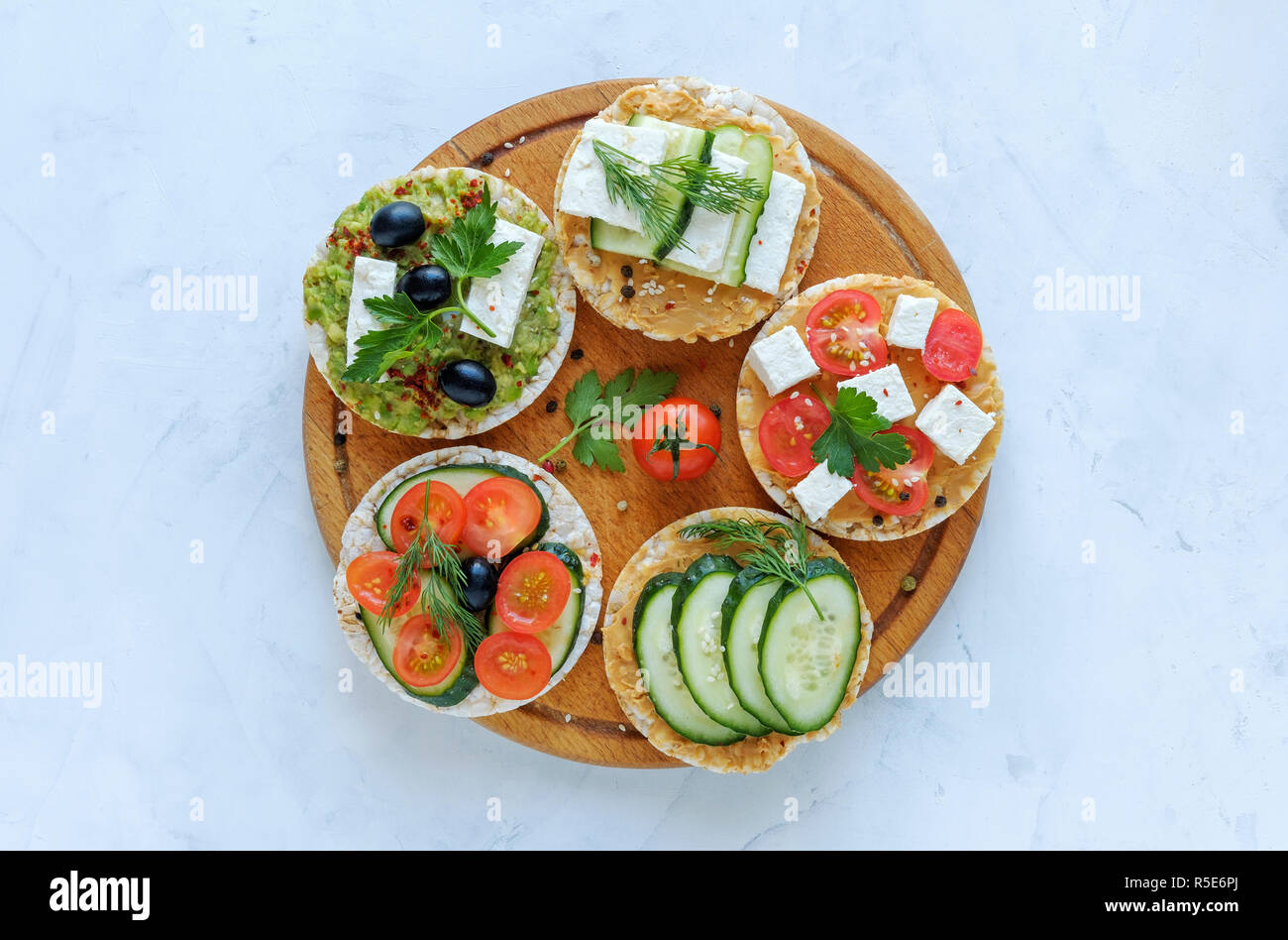 Homemade delicious appetizers on rice cakes with fresh veggies, feta cheese, herbs and boiled egg served on a wooden board over blue Stock Photo