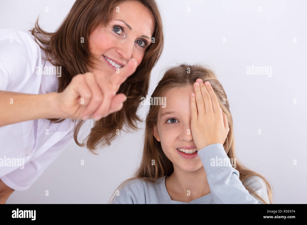 Smiling Female Optometrist Assisting Girl While Checking Eyesight In Clinic Stock Photo