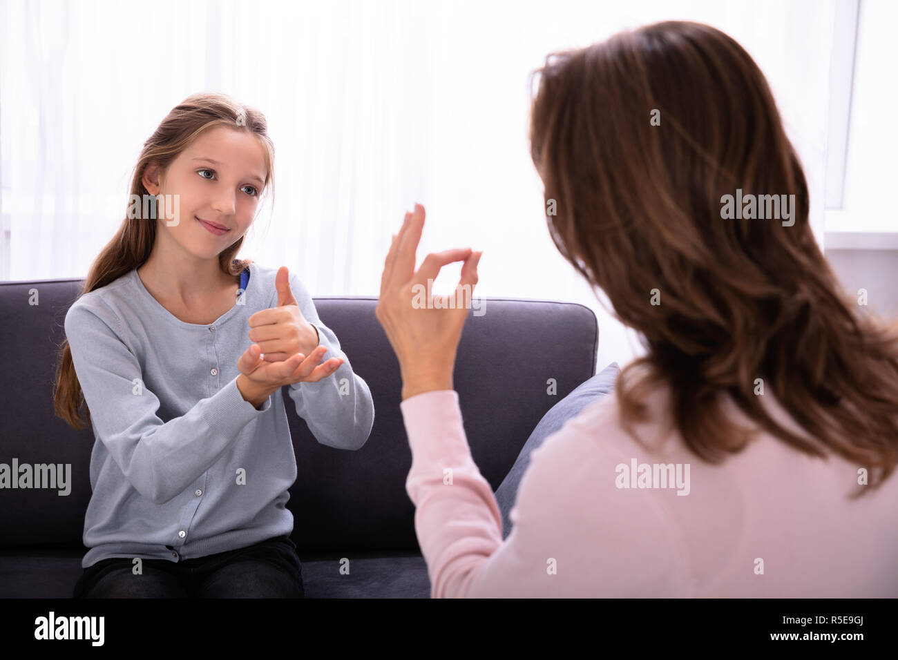 Happy Girl Sitting On Sofa Learning Sign Languages From Woman Stock Photo