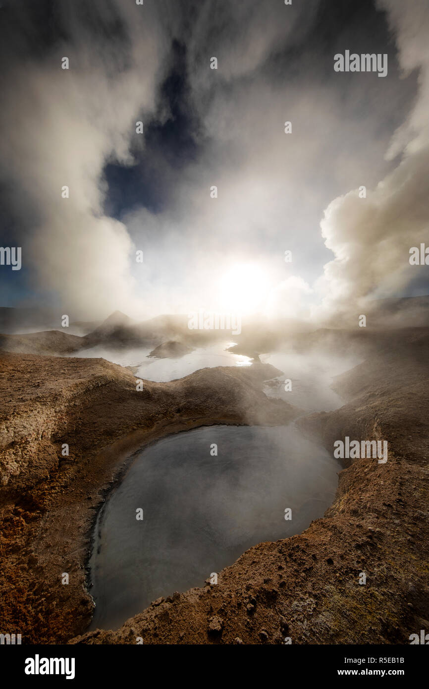 The Sun Rising through the Steaming Pools at Sol de Mañana Geothermic field Stock Photo