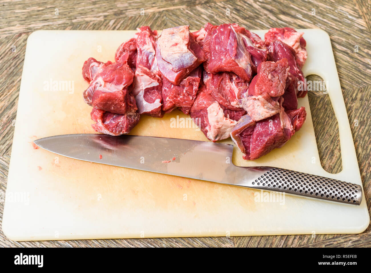 Pile of cut raw meat (chuck part) and knife on cutting board. Stock Photo
