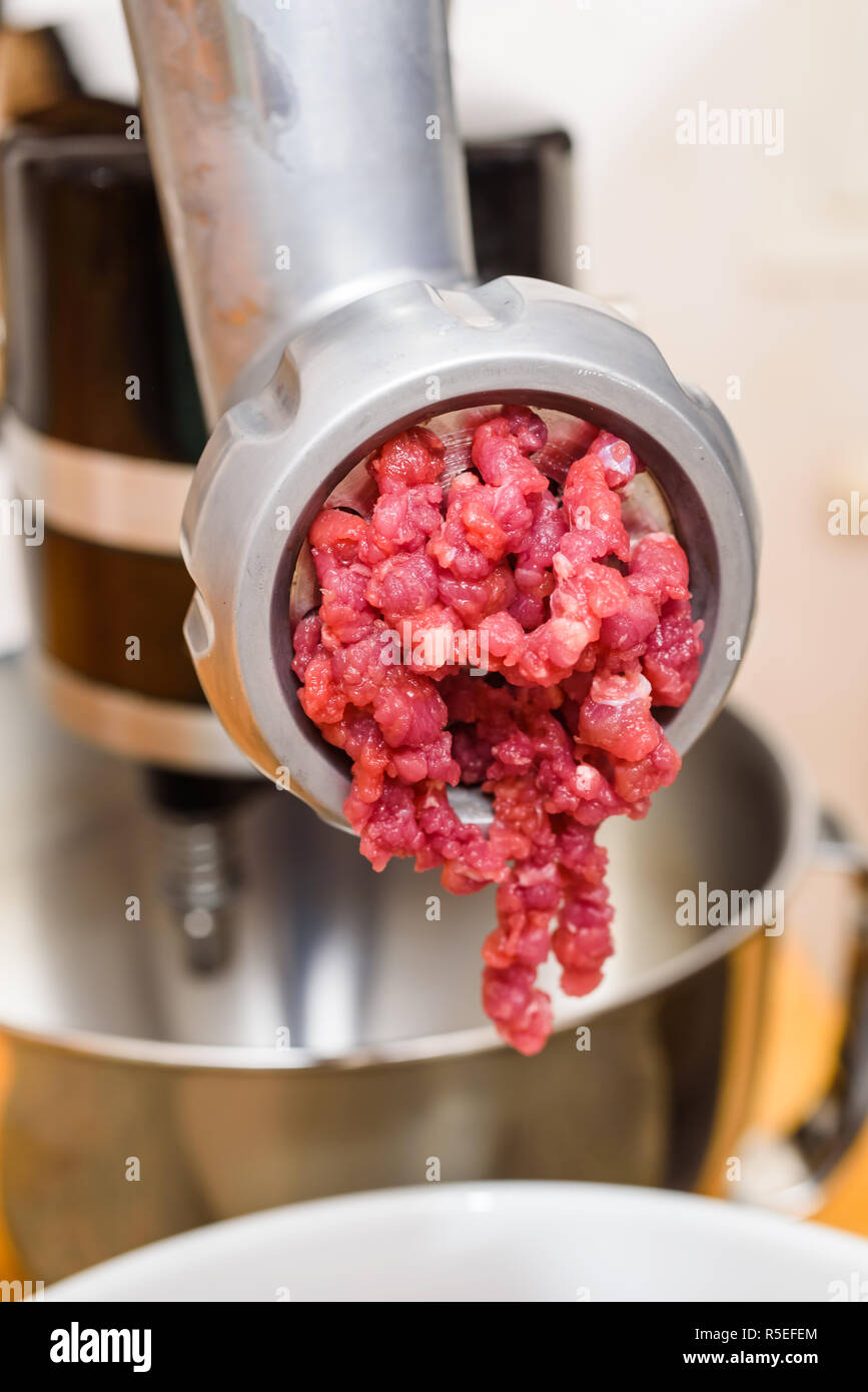 Raw meat coming out of the meat grinder as it is being minced. Stock Photo