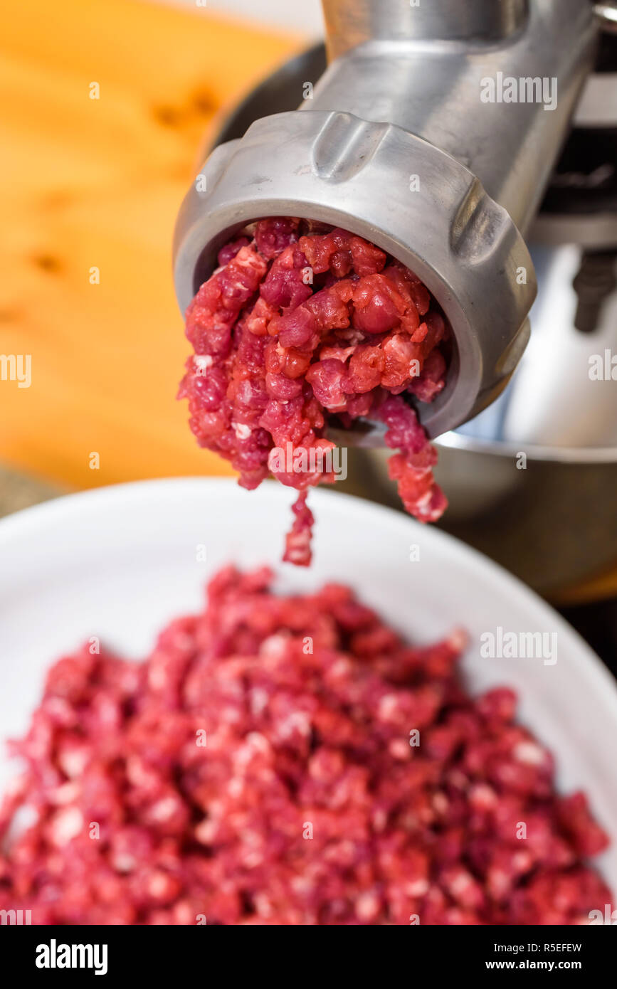 Raw meat coming out of the meat grinder as it is being minced. Stock Photo