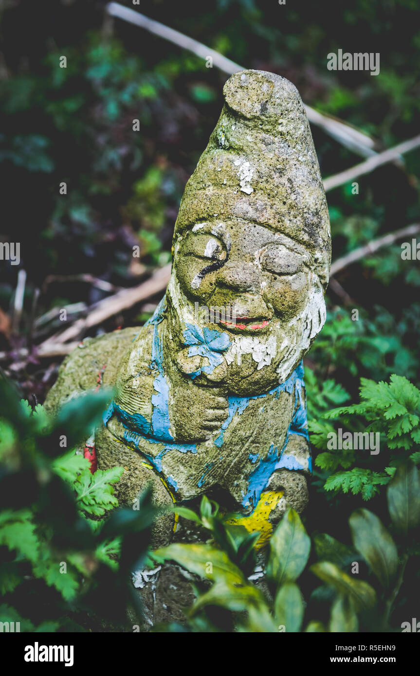 Weathered Garden gnome holding a faded blue flower - Colour photo Stock Photo