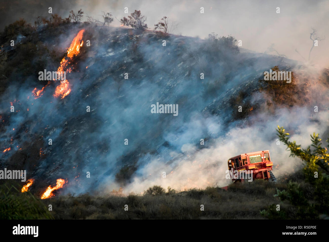 Wildfire flames burn hillside brush with dramatic shapes and color in California's Woolsey Fire.  Bulldozer in foreground during firefight. Stock Photo