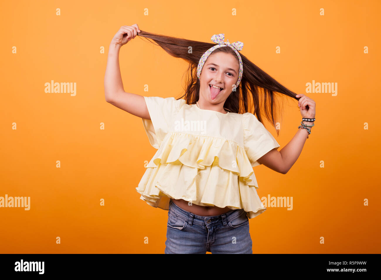 Little girl playing with her hair on a photoshoot in studio on yellow ...