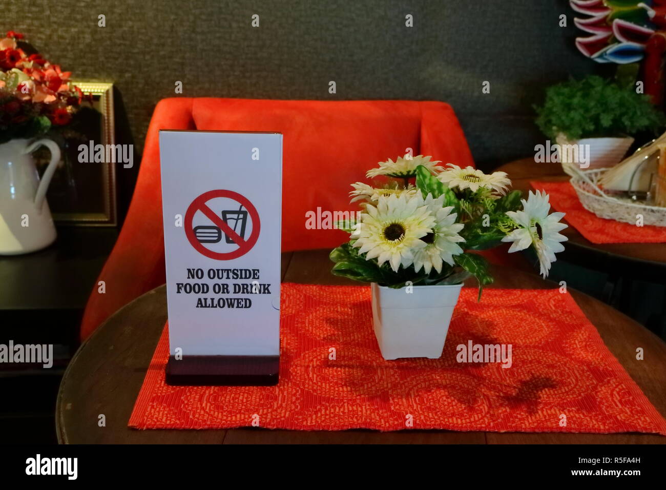 closeup of rectangular sign read no outside food or drink allowed, on red cloth with artificial flowers on round wooden table Stock Photo