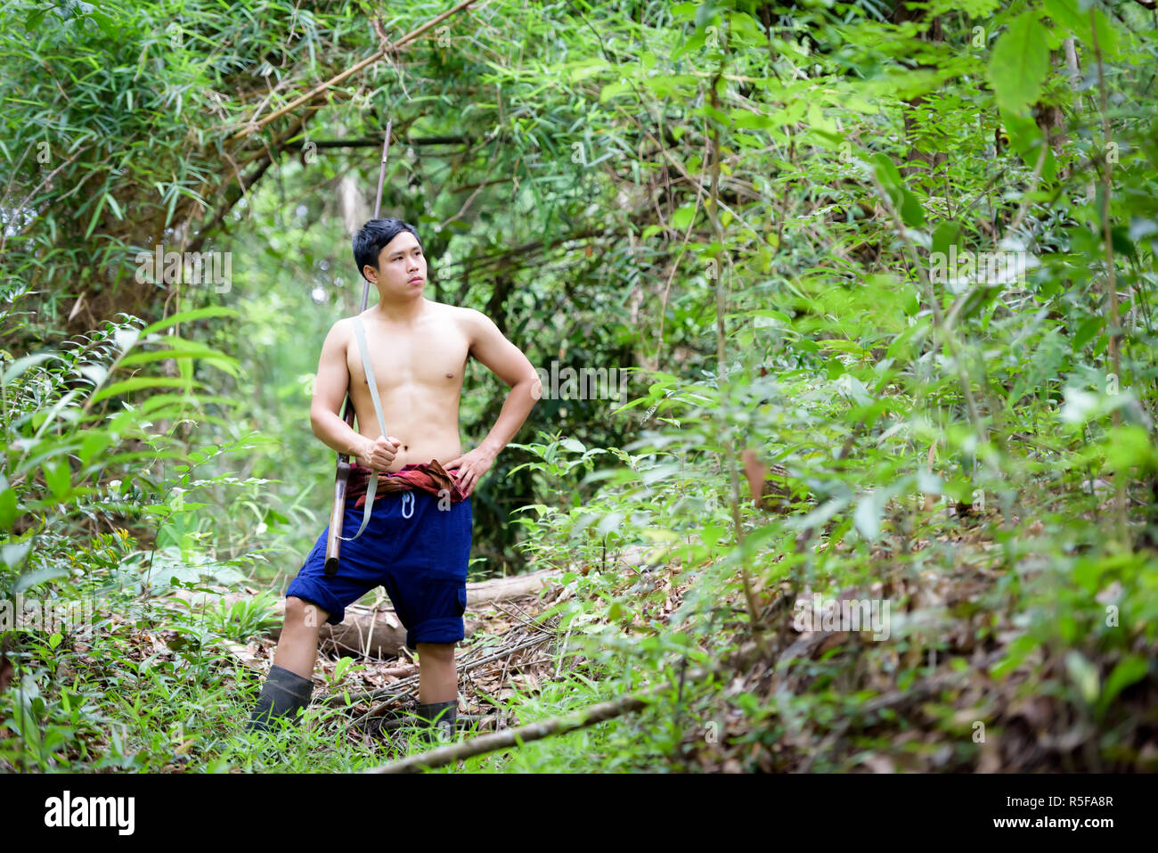 Asian man farmer carrying a rifle walks along in the forest background. Hunting and the way of life of rural people in Thailand concept. Stock Photo