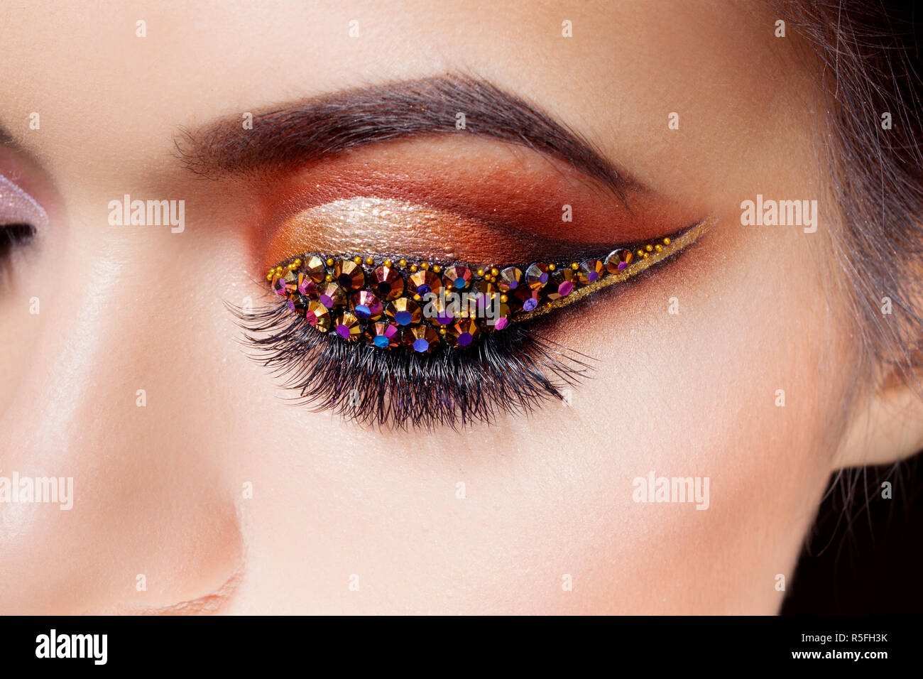 Amazing Bright eye makeup with a arrow with rhinestones. Brown and gold tones, colored eyeshadow. Close up. Stock Photo