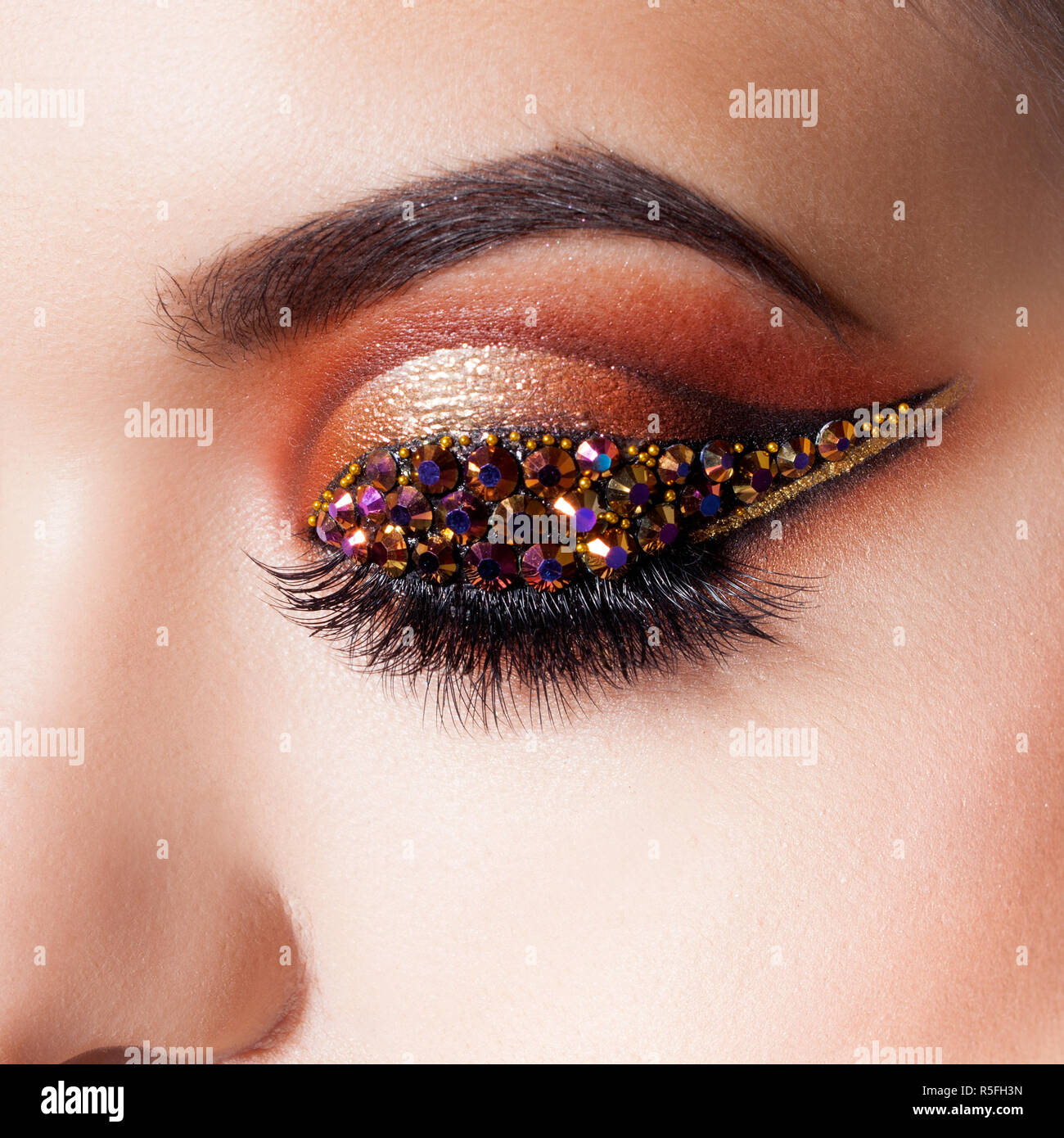 Amazing Bright eye makeup with a arrow with rhinestones. Brown and gold tones, colored eyeshadow. Close up. Stock Photo
