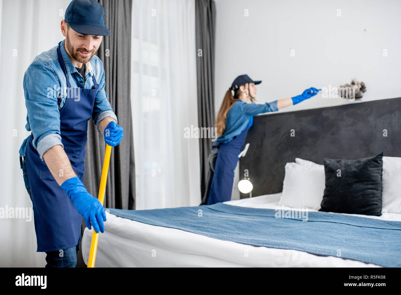 Professional cleaners in uniform washing floor and wiping dust from the