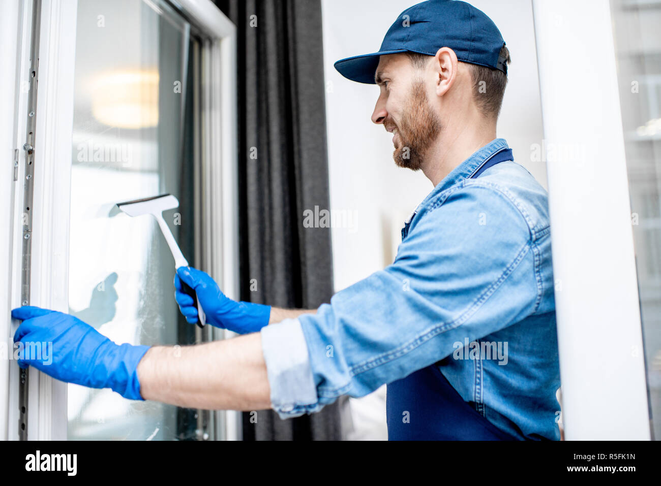 Man as a professional cleaner in blue uniform washing window with