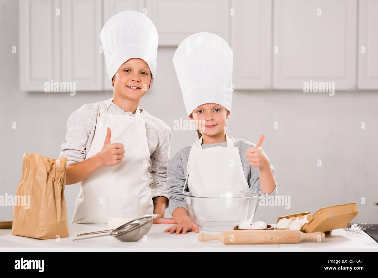 adorable brother and sister in chef hats showing thumbs up during food ...