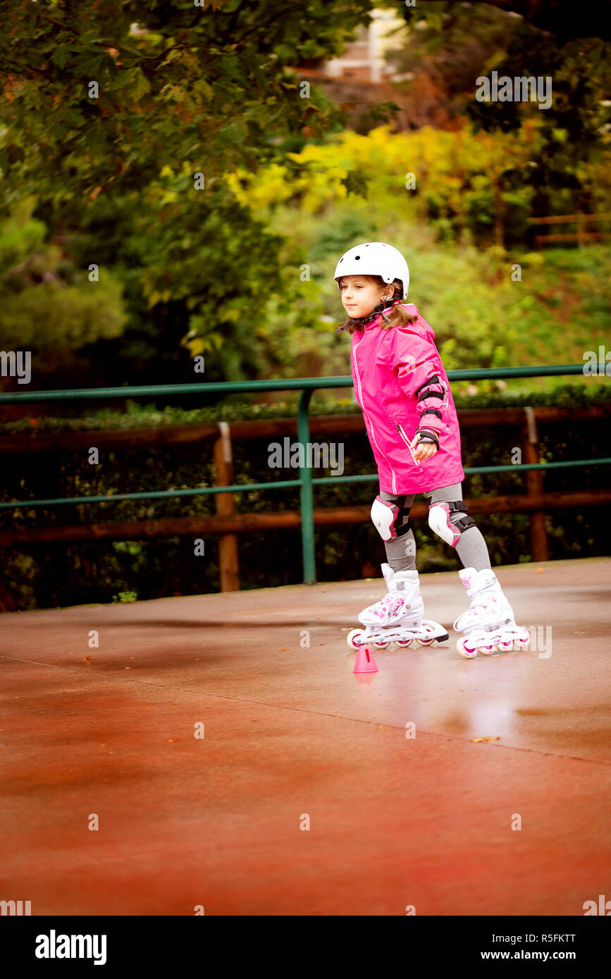 A little caucasian girl beginner roller in the autumn park in the rainy day. Stock Photo