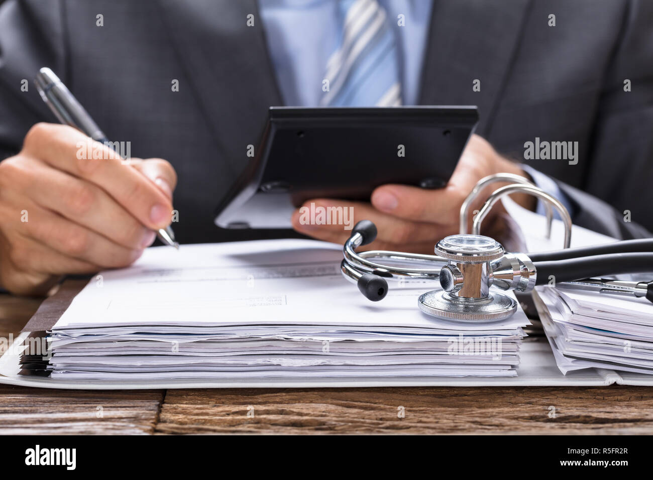 Businessman Calculating Invoice With Stethoscope On Documents Stock Photo