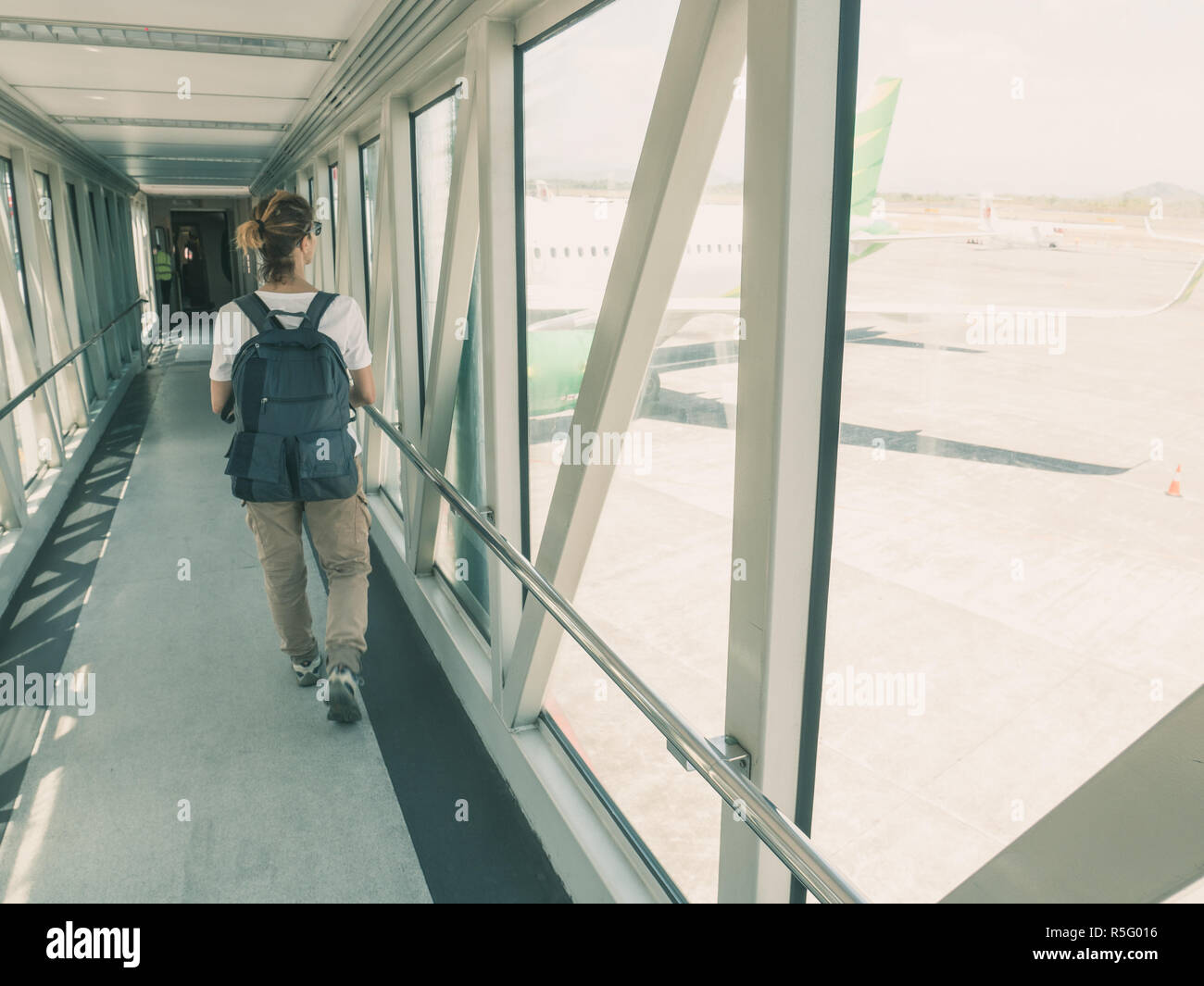 Woman backpacker walking to gate for departure in airport terminal. Window view ariplane waiting, toned, sunny day. Stock Photo