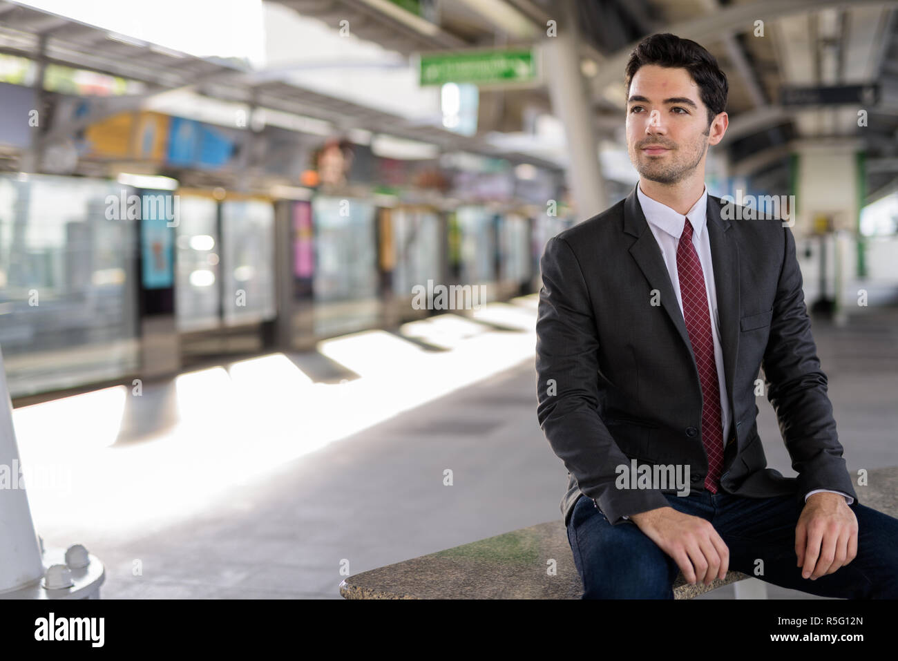 Portrait of young handsome businessman sitting at train station Stock Photo