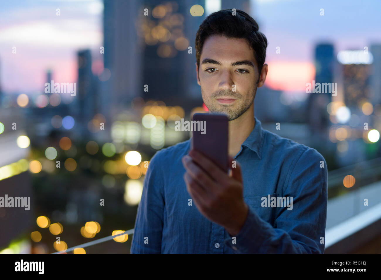 Portrait of man outdoors at night in city using mobile phone Stock Photo