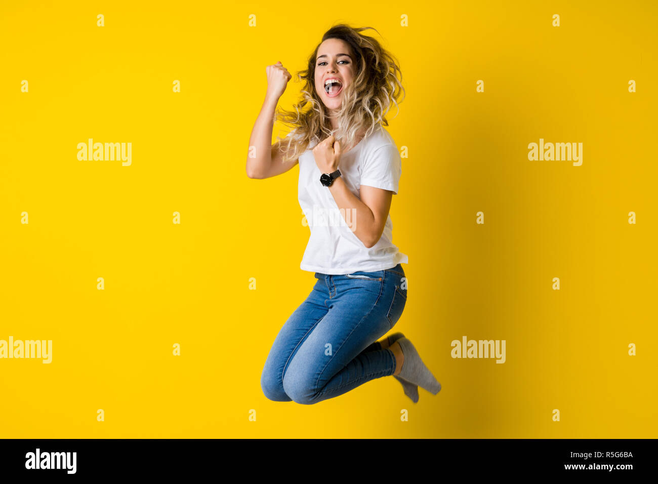 Beautiful young blonde woman jumping happy and celebrating with raised ...
