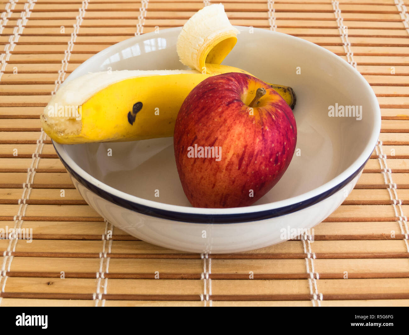 Apple and banana inside bowl on wooden stripes table Stock Photo