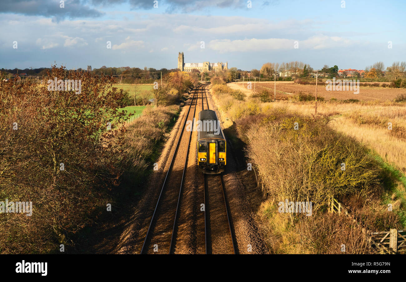 A railway train cuts through rural landscape on a bright autumn day with ancient minster on horizon near Beverley, Yorkshire, UK. Stock Photo