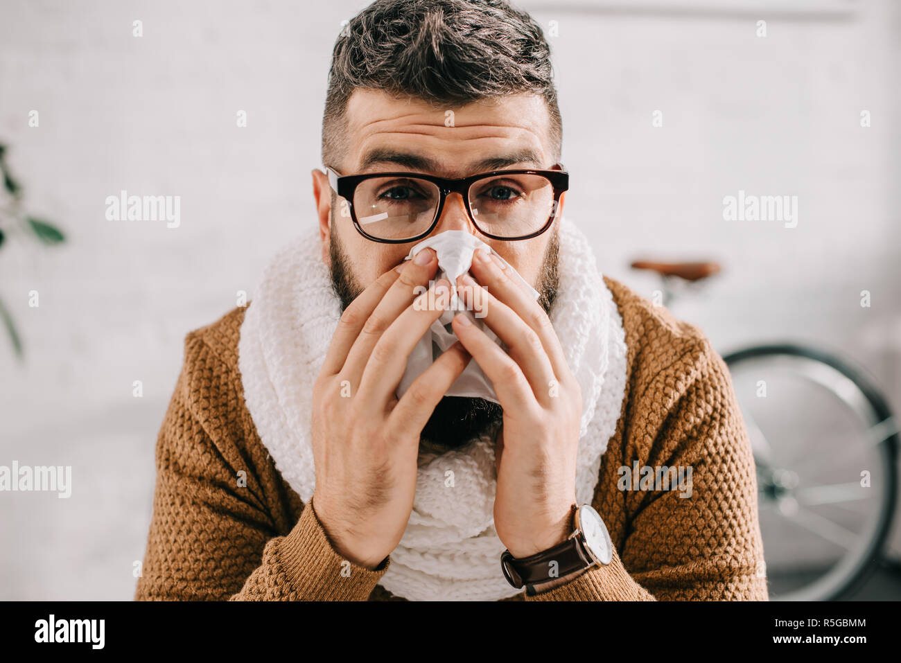 portrait of sick man in knitted scarf sitting in office, sneezing and ...