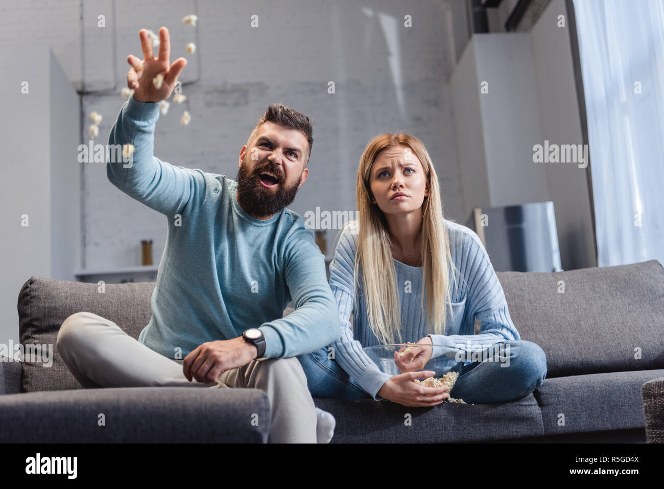 Emotional husband throwing popcorn and sitting on sofa with wife Stock Photo Alamy