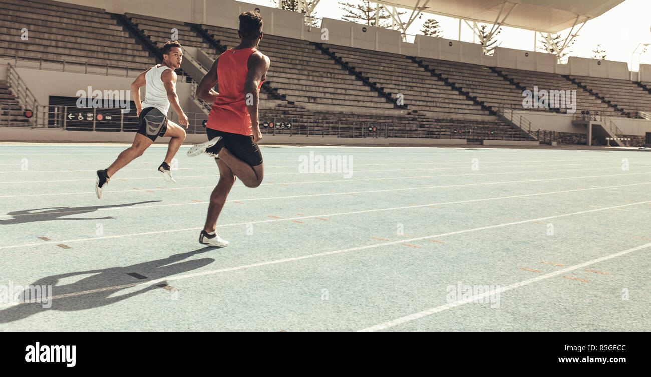 Two men running a race on a running track on a sunny day. Athletes training on a race track competing with each other. Stock Photo