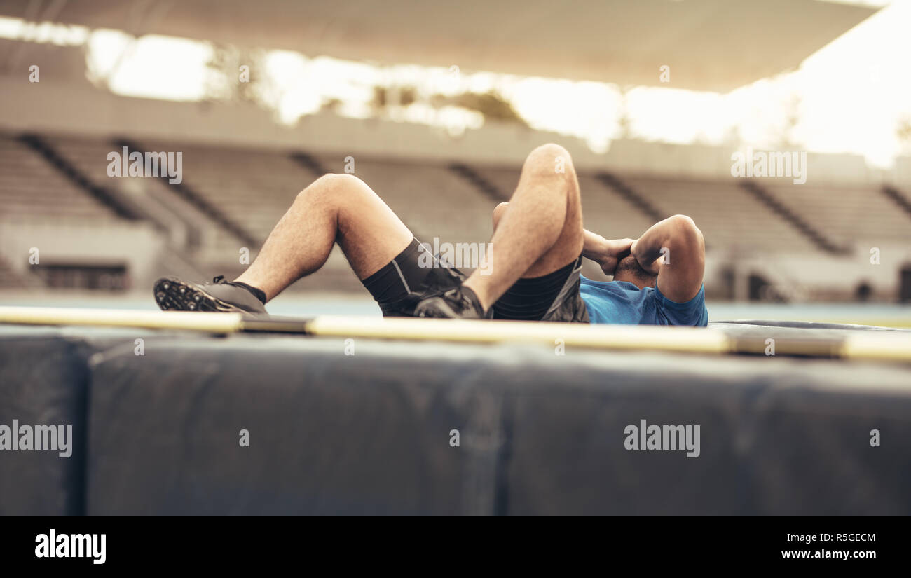 Athlete falling on the high jump landing mat. Athlete holding his hands to his face lying on landing mat after a high jump. Stock Photo