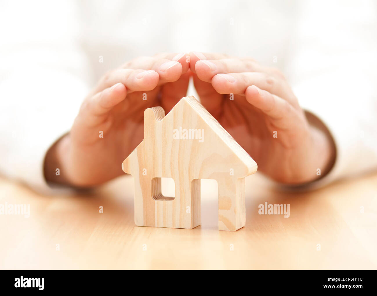 Wooden toy house protected by hands Stock Photo