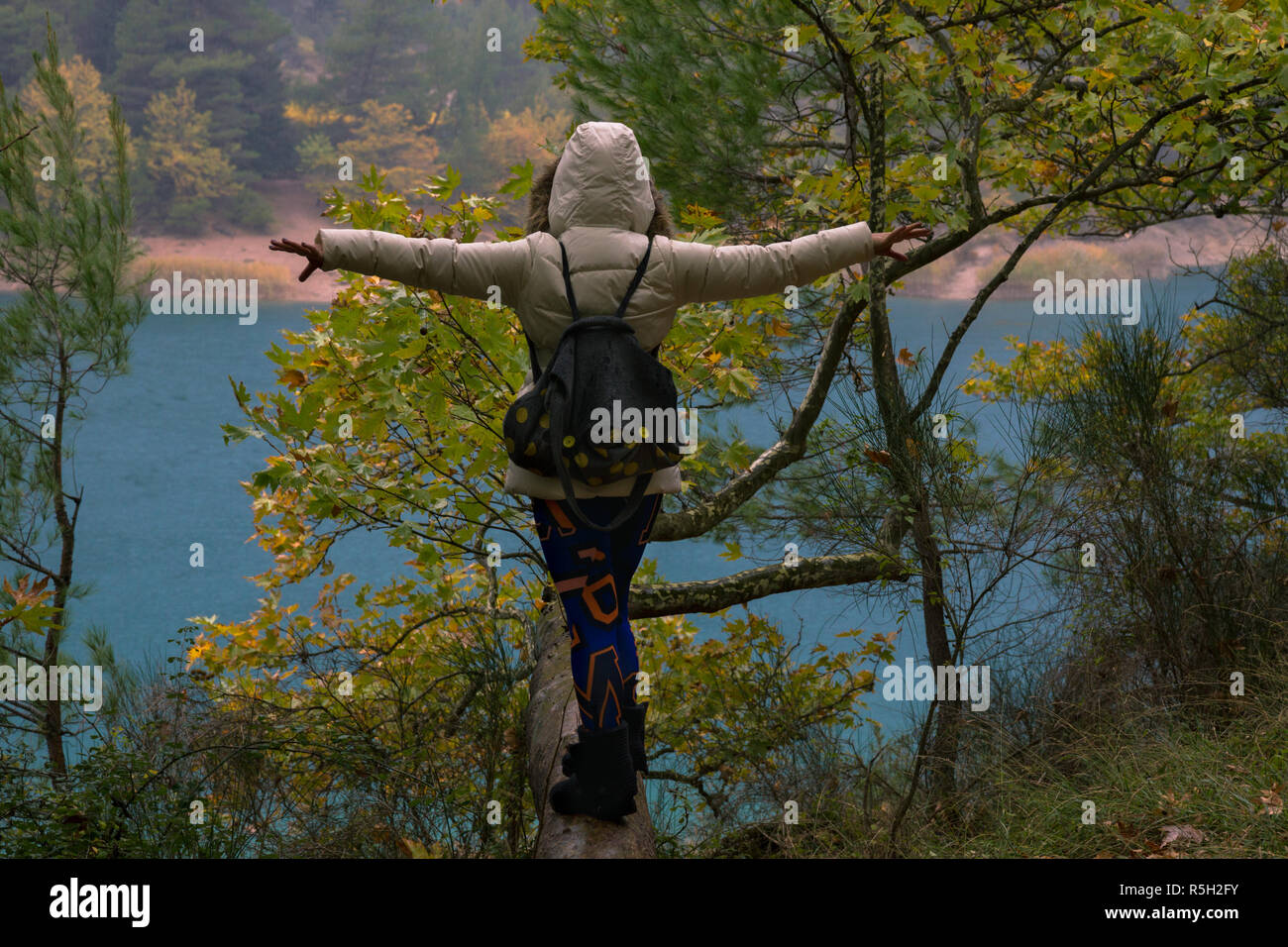 A woman in lake Tsivlos balancing on a tree log, on a rainy day. Stock Photo
