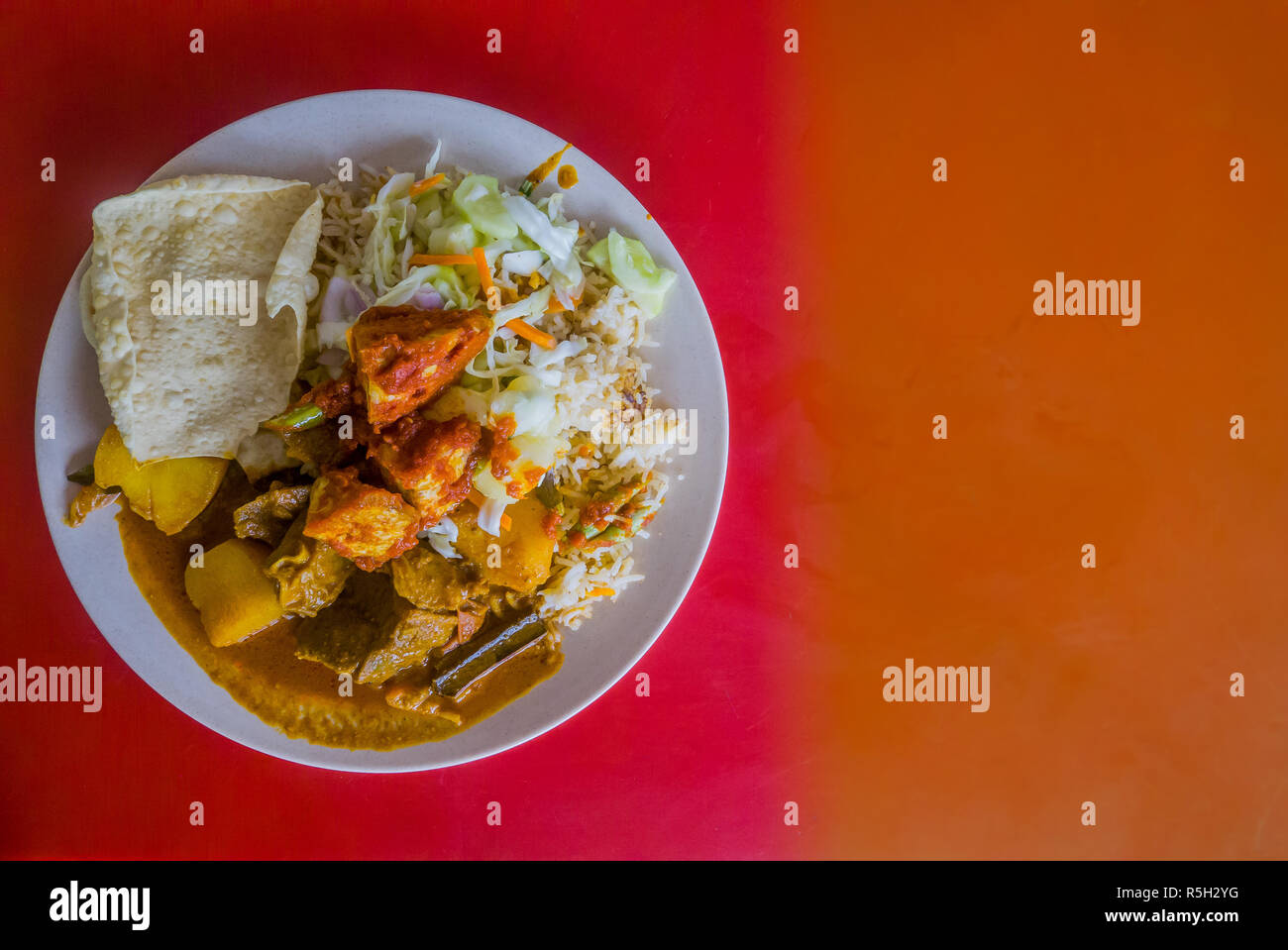 Authentic Indian food from family street restaurant. Isolated plate on red background with dark orange section for text. Delicious Stock Photo