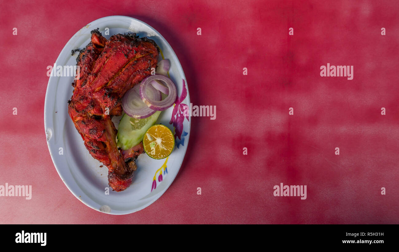 Authentic Indian - Malaysian food from family street restaurant. Spicy Tandoori chicken plate isolated on red background. Delicious Stock Photo