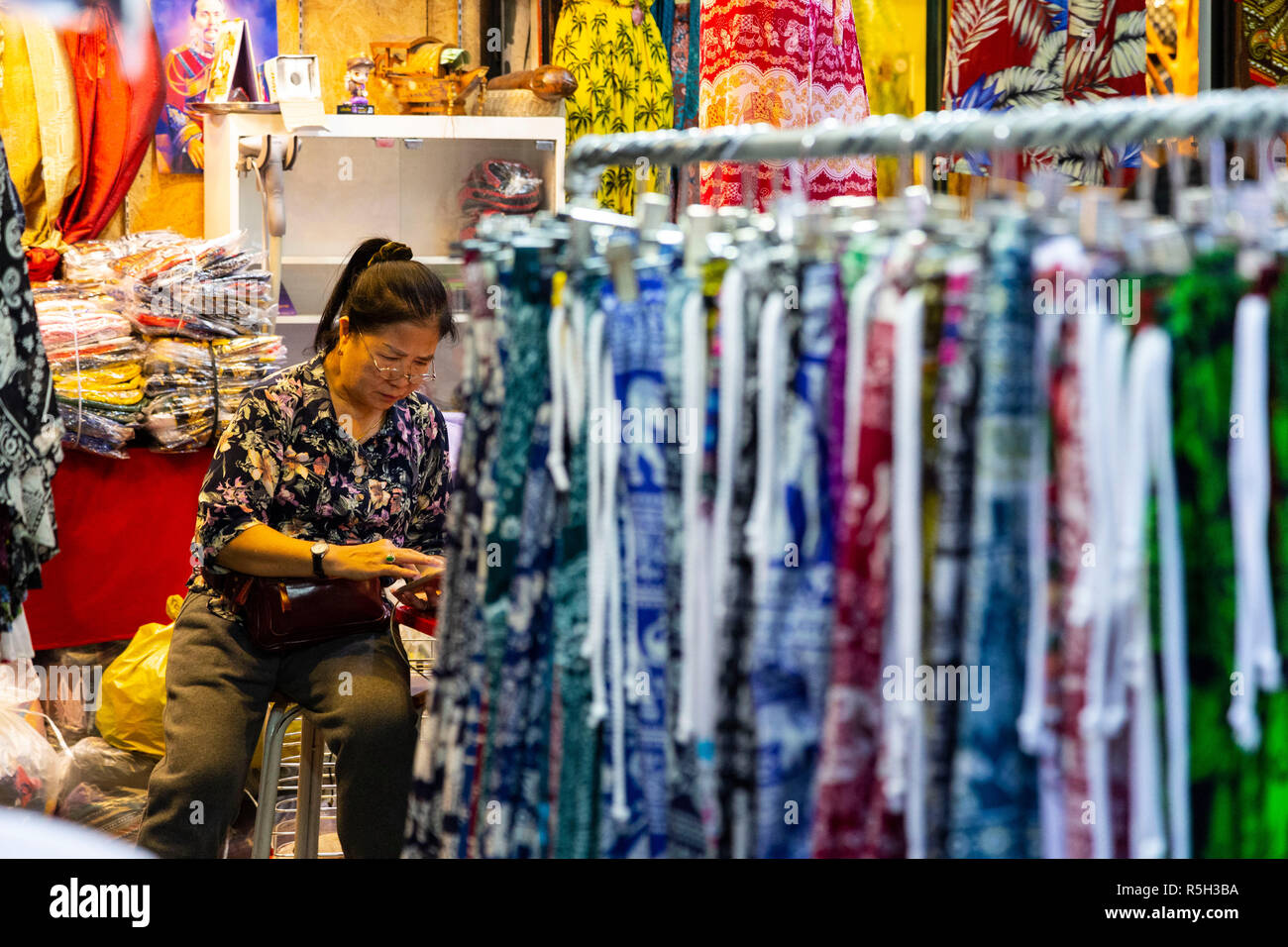 aleswoman sitting in a clothing store with very colorful clothes and waiting for tourists Stock Photo