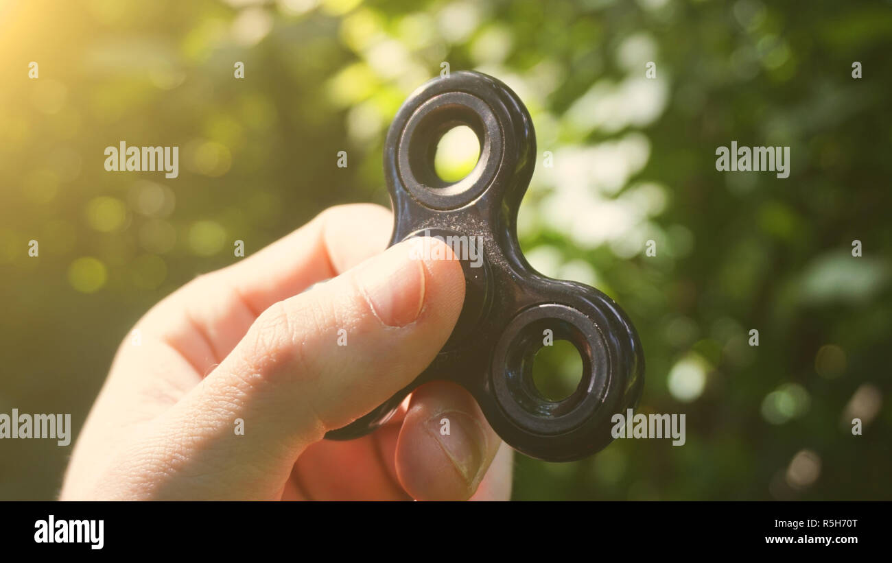 Playing with the black Fidget Spinner. Toy spinner in hand. Sun effect Stock Photo