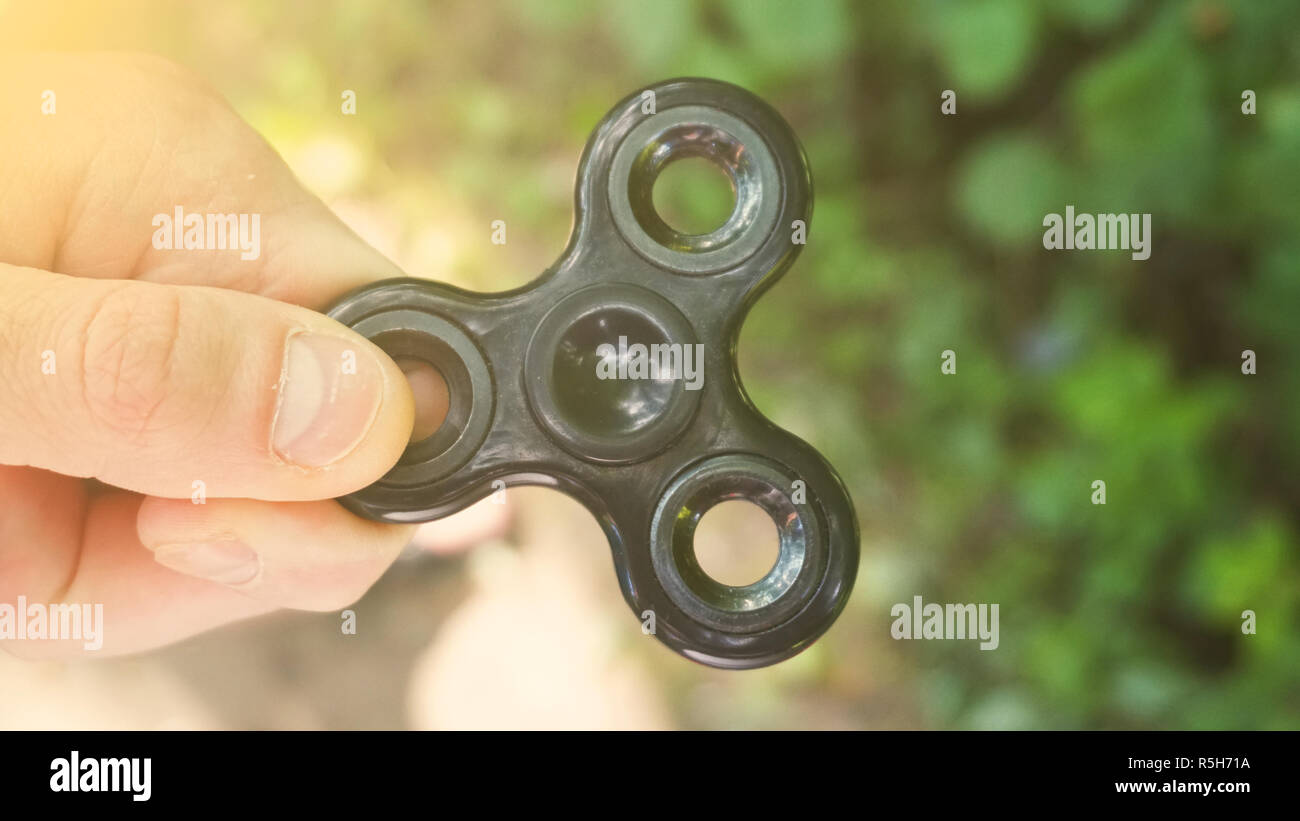 Playing with the black Fidget Spinner. Toy spinner in hand. Sun effect Stock Photo