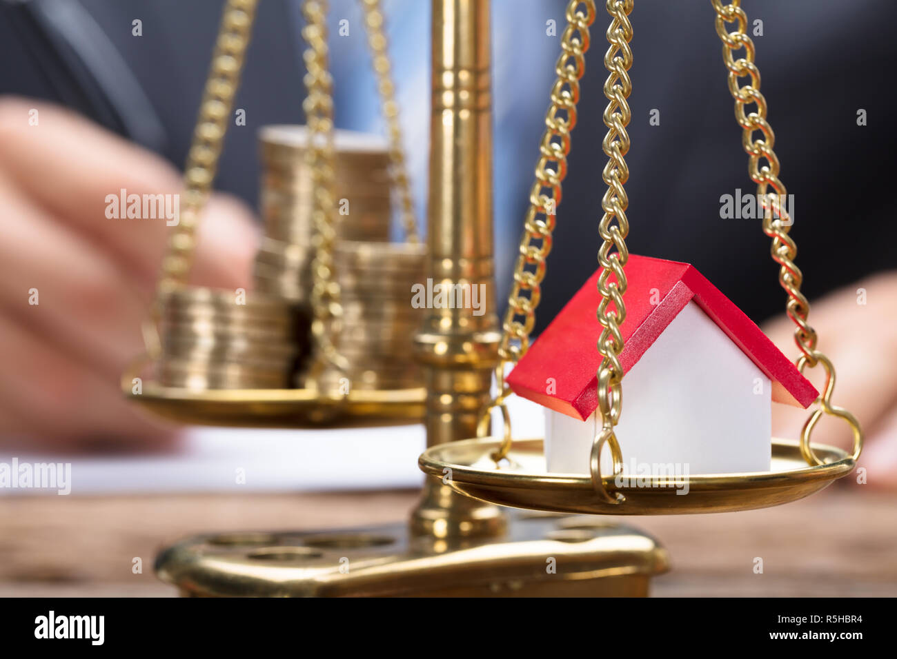 Businessman With Model Home And Coins On Golden Weighing Scale Stock Photo