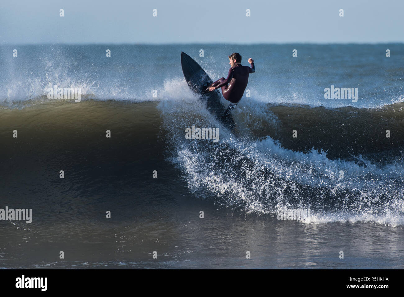 Bearded surfer in black wetsuit flying across wave face and off the lip on a 6 foot set wave in Ventura, California, USA on December 1, 2018. Stock Photo