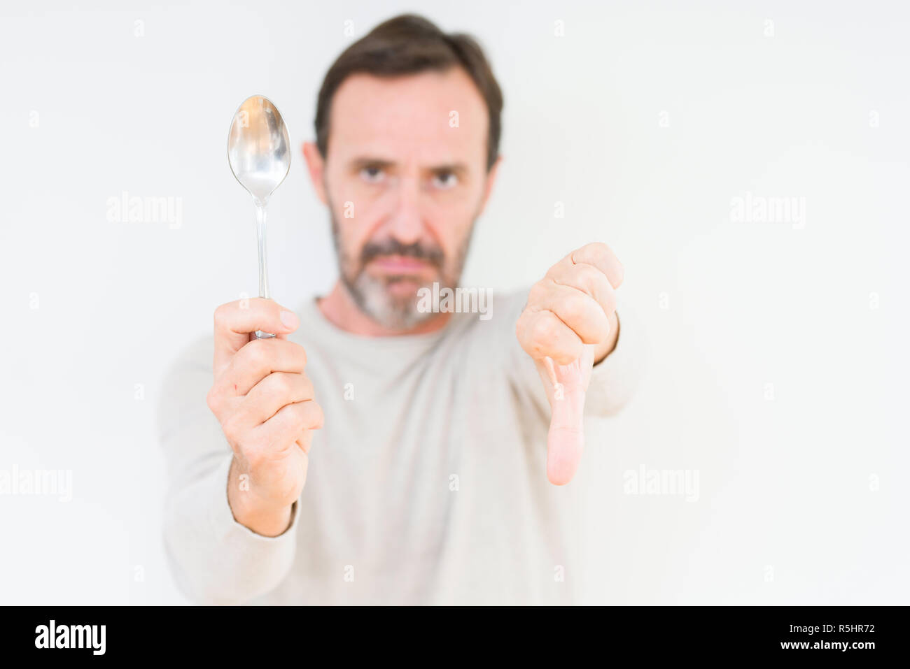 Senior man holding silver spoon over isolated background with angry ...