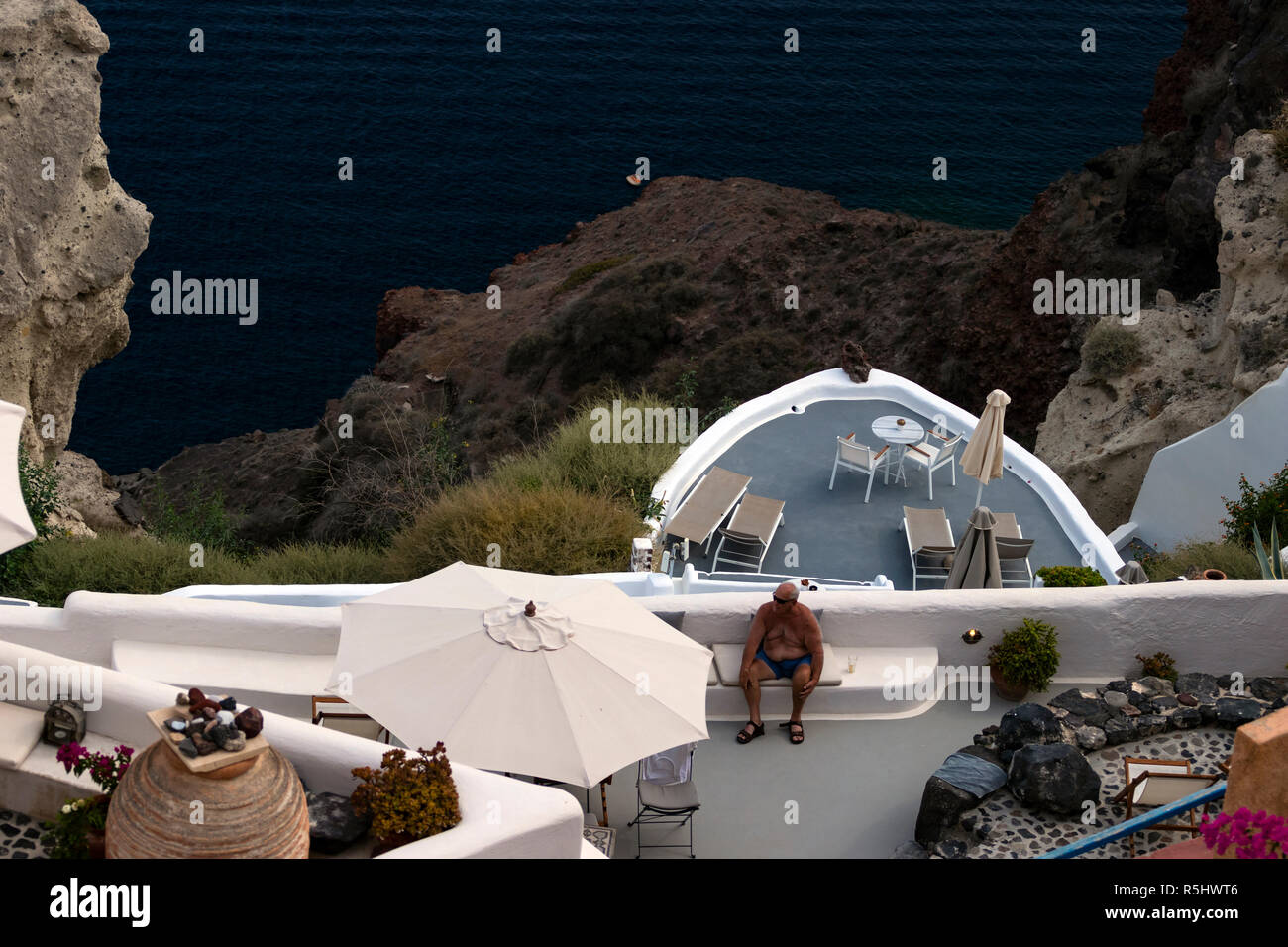 OIA, SANTORINI, GREECE - August 28, 2018: Wealthy retired tourist leisurely sits by the pool in an exclusive cliff side suite. Stock Photo