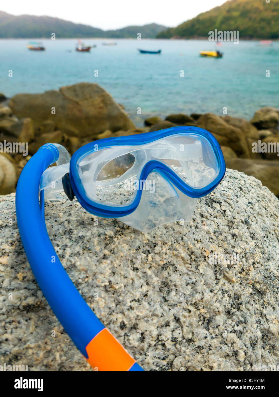 Snorkeling equipment: snorkel and diving google on the stone. Tropical island, sea, beach and boats in background. Stock Photo